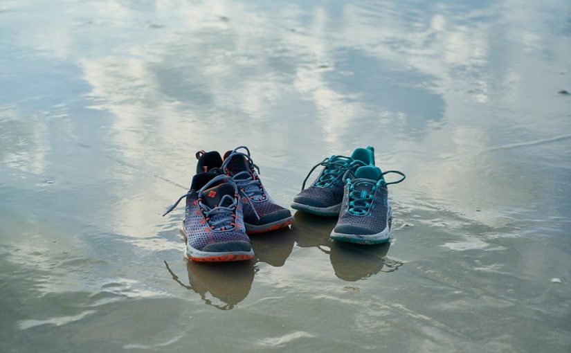 沙滩上的两双鞋的照片。它们的倒影被捕捉在沙滩上的水层中。