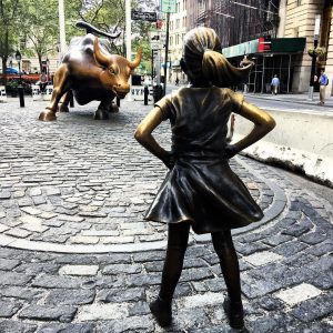 纽约无畏女孩雕像的照片。雕像是一个年轻的女孩，双手叉腰站着，面对着一个巨大的公牛雕像。