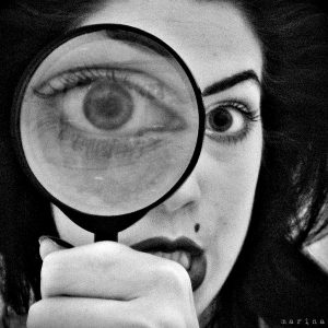一个女人透过放大镜看东西的照片。结果一只眼睛变大了。
