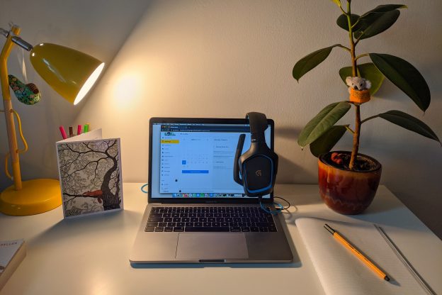 Macbook pro放在白色的桌子上，旁边有一棵植物和黄色的台灯