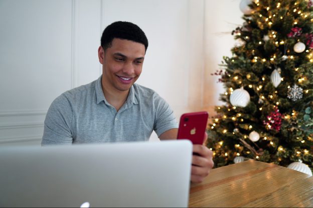 一名男子在他的笔记本电脑和iphone上工作，背景是圣诞树-不飞溅
