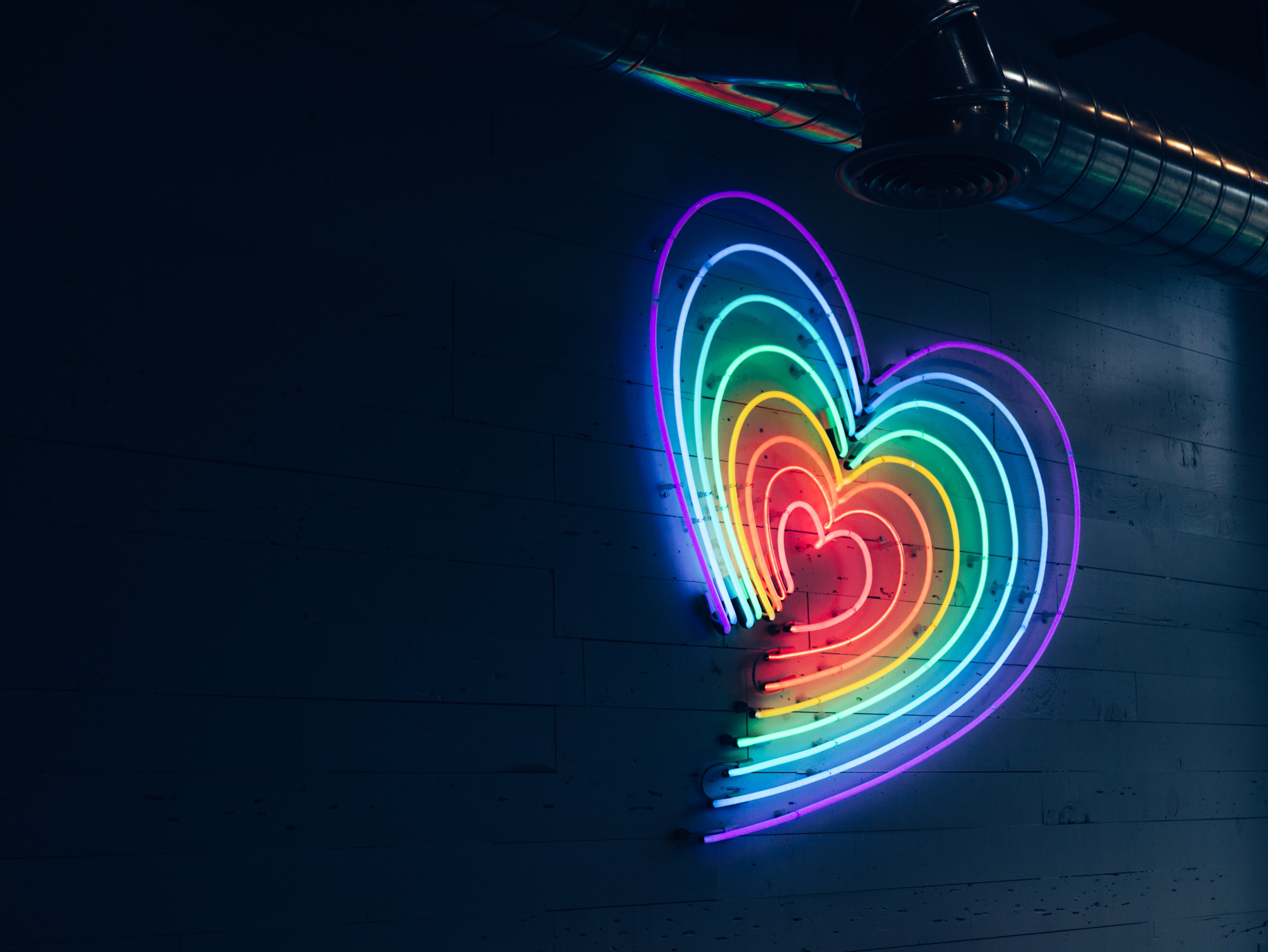 骄傲月-霓虹灯在一个彩虹颜色的心形靠墙设置