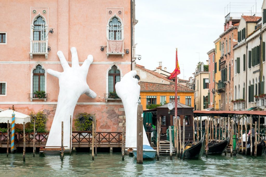 巨大的白色雕刻的手，伸出运河，支撑着一座高楼。