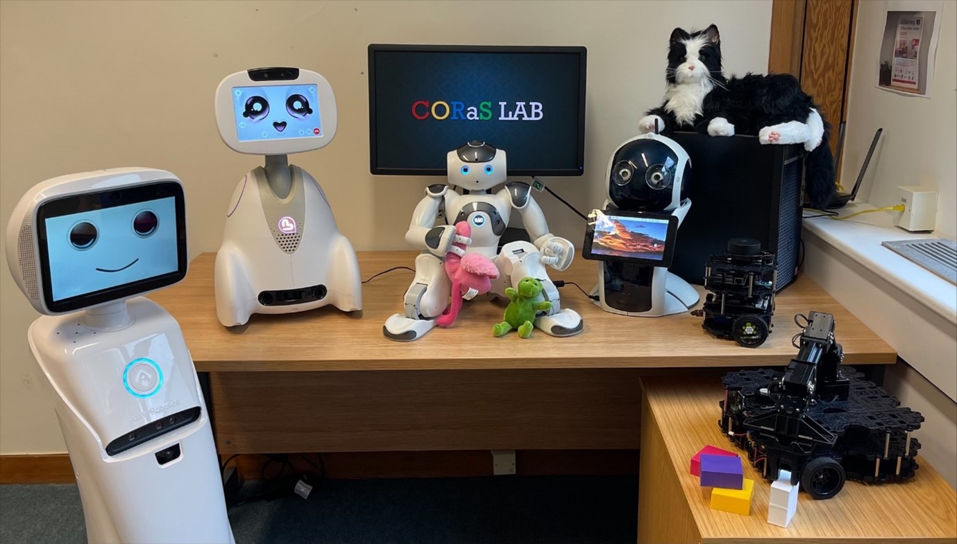 桌子上的电脑显示器上，屏幕上写着“科拉斯实验室”，周围是机器人和毛绒玩具