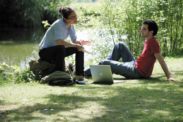 两个人坐在校园的池塘边