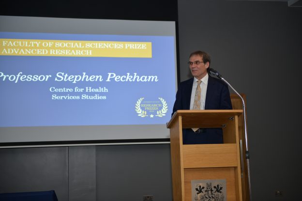 Stephen Peckham教授站在讲台上，在他身后的投影仪屏幕上说:社会科学学院奖和高级研究教授Stephen Peckham健康服务研究中心