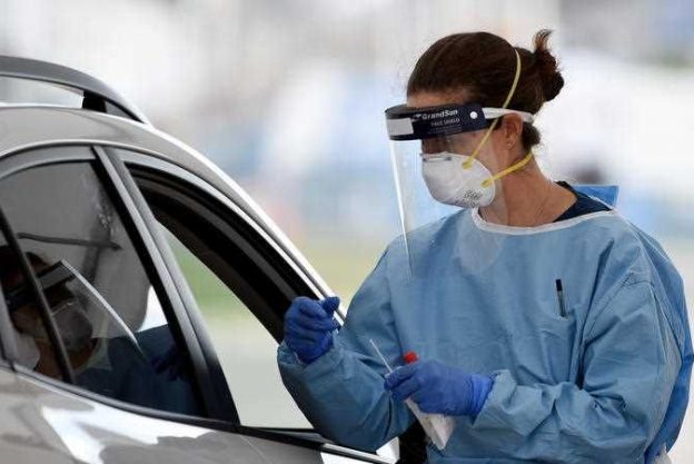 A medic person in PPE testing someone sitting in their car.