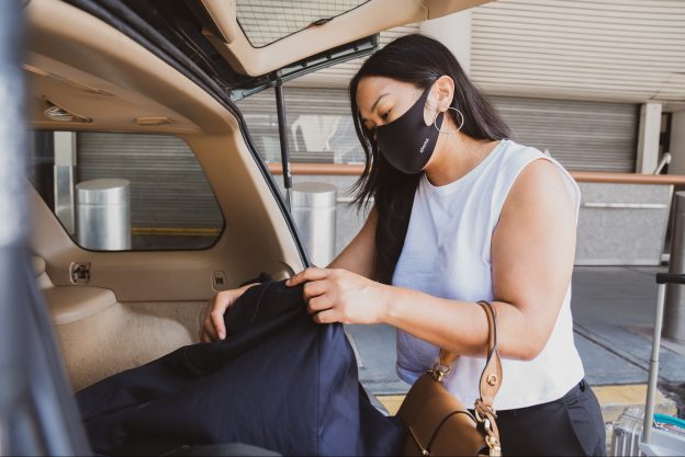 一个穿着白色背心戴着面具的女人把一个包放在车后备箱里