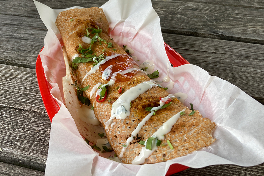 A basket filled with a vegetable dosa and drizzled with mint yogurt